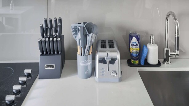 Uma cozinha com armários brancos, uma pia de aço inoxidável e uma torradeira no balcão.