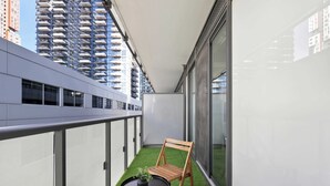 Uma varanda com uma mesa pequena, uma cadeira, um vaso de planta e vista para um edifício alto.