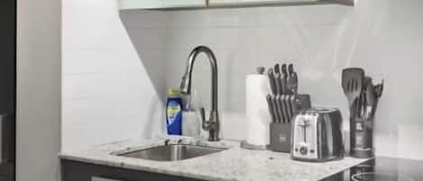 A modern kitchen with a marble countertop, stainless steel sink, and a range hood.