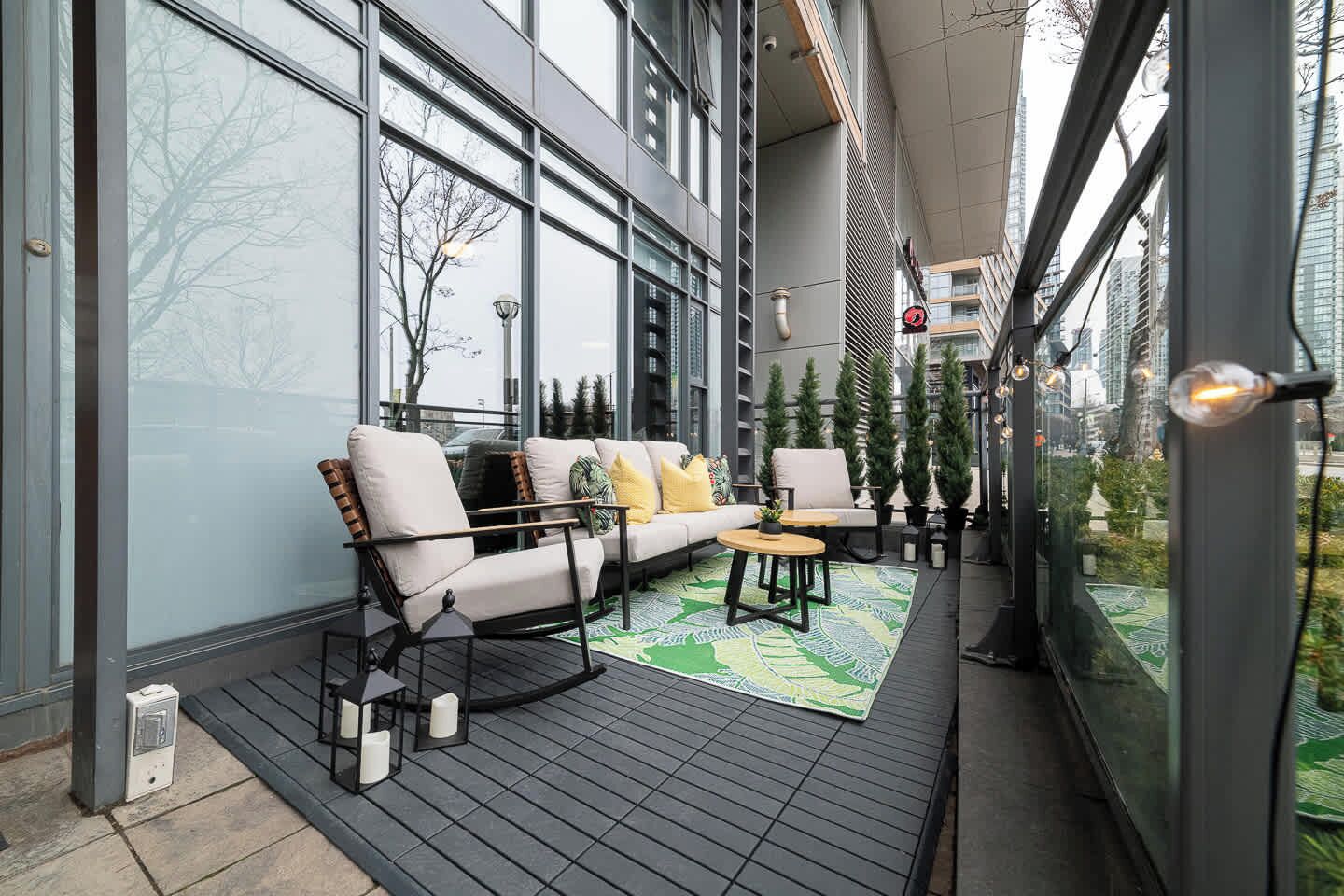 Un espace extérieur moderne aménagé avec un canapé et des fauteuils, un tapis à motifs et des plantes en pot.
