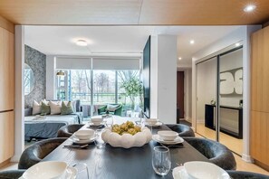 A modern dining area with a long table set for a meal, a sofa, and a large window providing a view of the outdoors. - Private Home, 3 BR, Rogers Centre & Free Parking (Toronto)