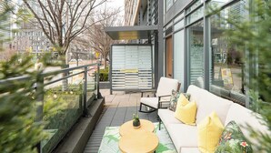 Een terras met een bank, stoelen en een kleine tafel, met uitzicht op een stadsweg.