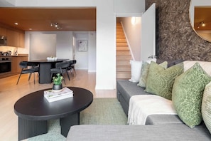 A modern living room with a dark coffee table, a grey sofa with patterned cushions, and a staircase leading to an upper floor. - Private Home, 3 BR, Rogers Centre & Free Parking (Toronto)