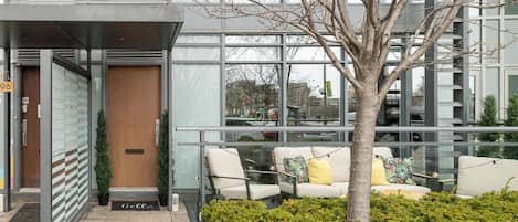 A modern building with a glass facade, a wooden door, and a seating area with cushions.