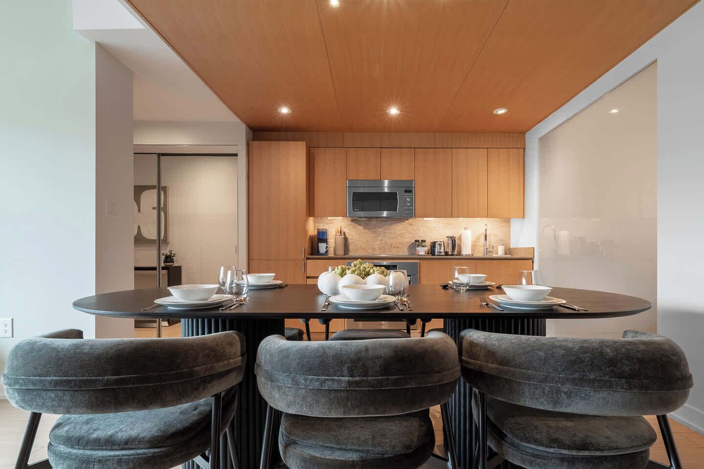 Une cuisine moderne avec des meubles en bois, un four à micro-ondes encastré et un coin repas comprenant une table ronde et des chaises rembourrées.