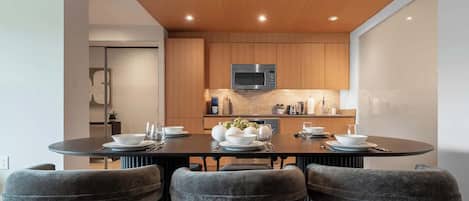 Una cocina moderna con armarios de madera, microondas integrado y comedor con mesa redonda y sillas tapizadas.