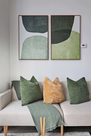 A sofa with a green throw blanket and four cushions in various shades of green and one in a beige tone.