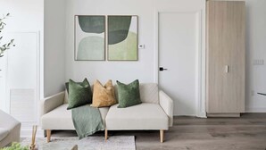 A modern living room with a sofa, cushions, a wall-mounted abstract art piece, a wooden wardrobe, and a door.
