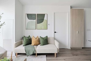 A modern living room with a sofa, cushions, a wall-mounted abstract art piece, a wooden wardrobe, and a door.