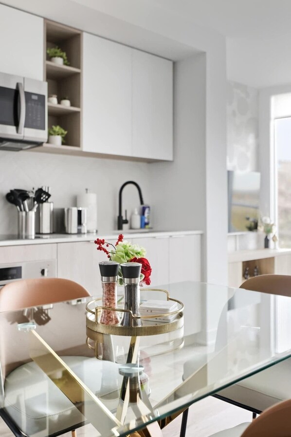 A modern kitchen with white cabinetry, a glass dining table, and a kitchen island with salt and pepper shakers and a vase of flowers.