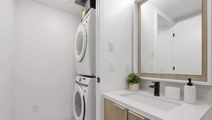 A modern bathroom with a built-in washer and dryer, a sink with a mirror, and a small potted plant.
