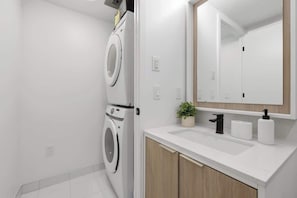 A modern bathroom with a built-in washer and dryer, a sink with a mirror, and a small potted plant.