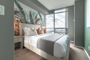 A modern bedroom with a large bed, a city view, and a tropical mural on the wall. - Chic Fort York Haven Lake Views & City Pulse (Toronto)