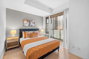 Ein modernes Schlafzimmer mit einem großen Bett, zwei Nachttischen, einem Beistelltisch und einem großen Fenster mit Blick auf Gebäude.