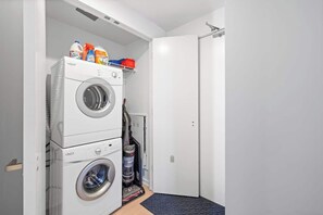 Ein Waschraum mit gestapelten Waschmaschinen, einem Staubsauger und Waschmittelbehältern.