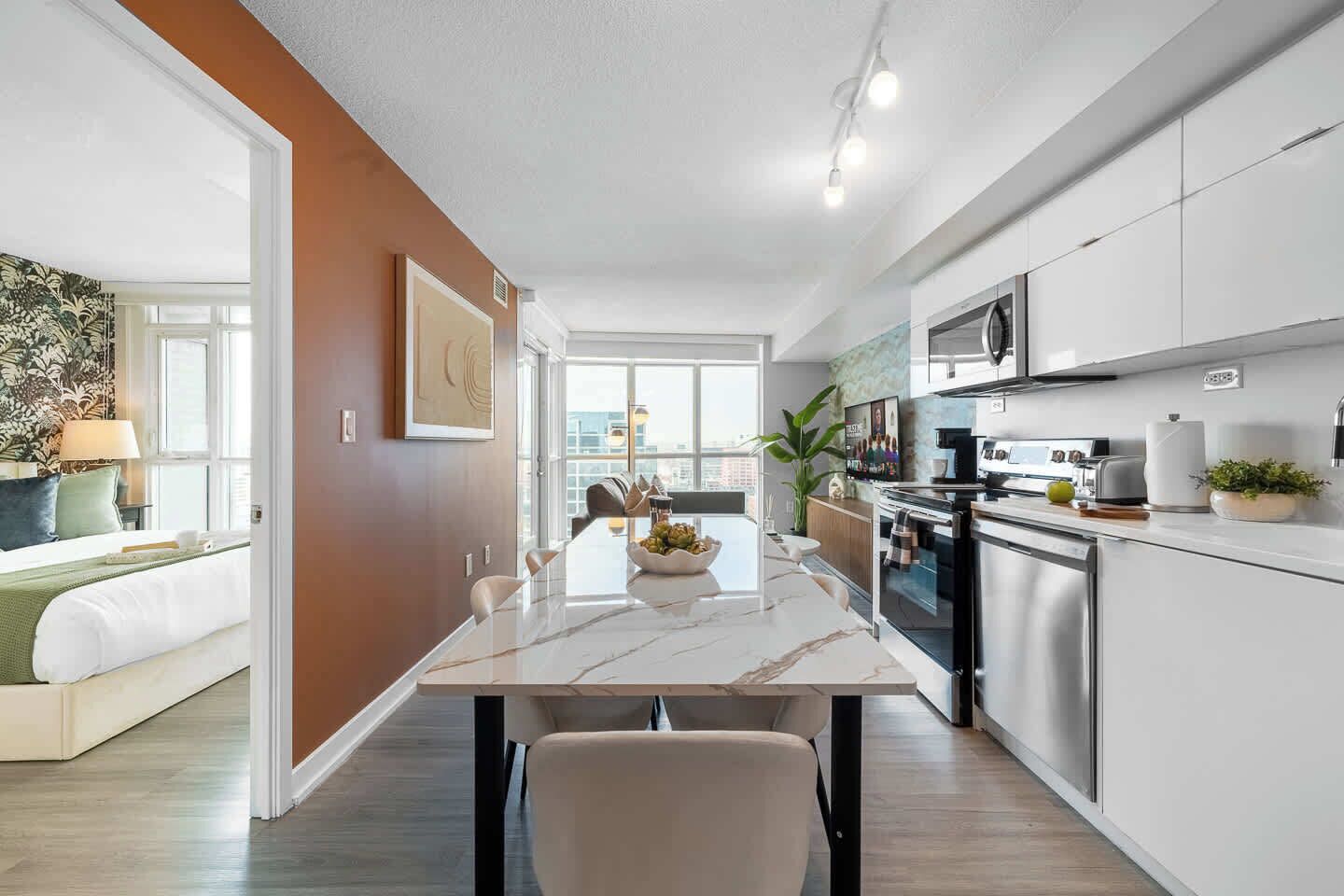 A modern kitchen with stainless steel appliances, a marble countertop, and a dining area with a view.