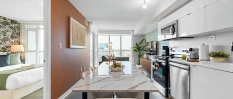 A modern kitchen with stainless steel appliances, a marble countertop, and a dining area with a view.