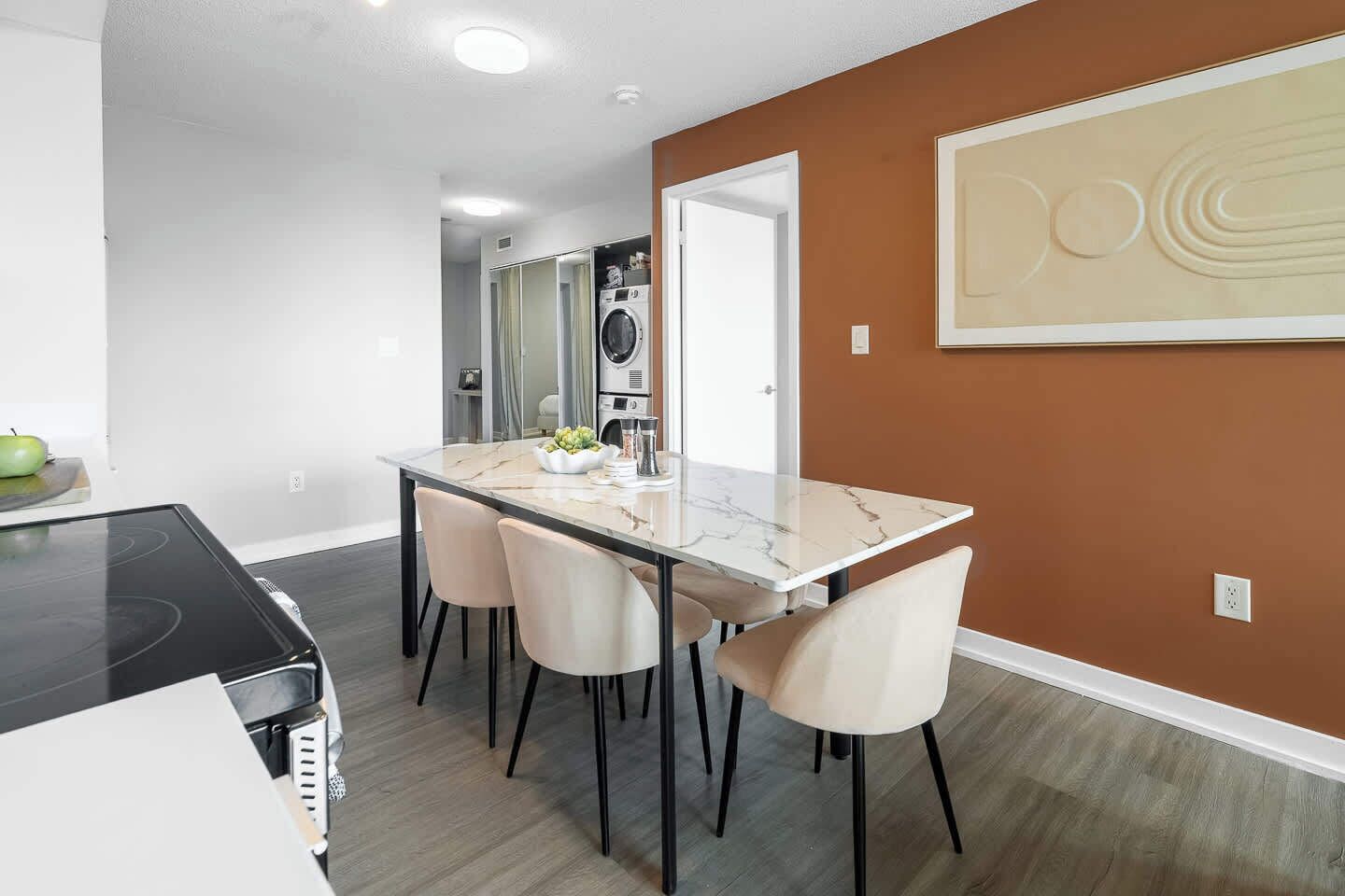 A modern kitchen with a black countertop, a dining table with four chairs, and a wall-mounted oven.