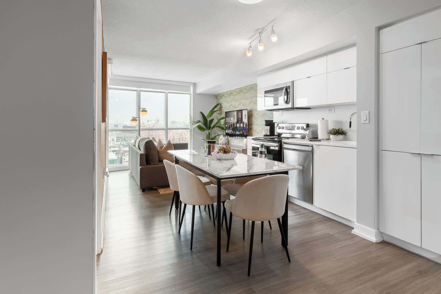 Una cocina moderna con armarios blancos, una mesa de comedor con sillas y un ventanal con vistas a la ciudad.