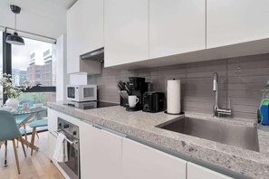 A modern kitchen with a large window, a built-in microwave, a coffee maker, and a stainless steel sink. - Chic City Oasis with Cafes & Bars at your Doorstep! (Toronto)