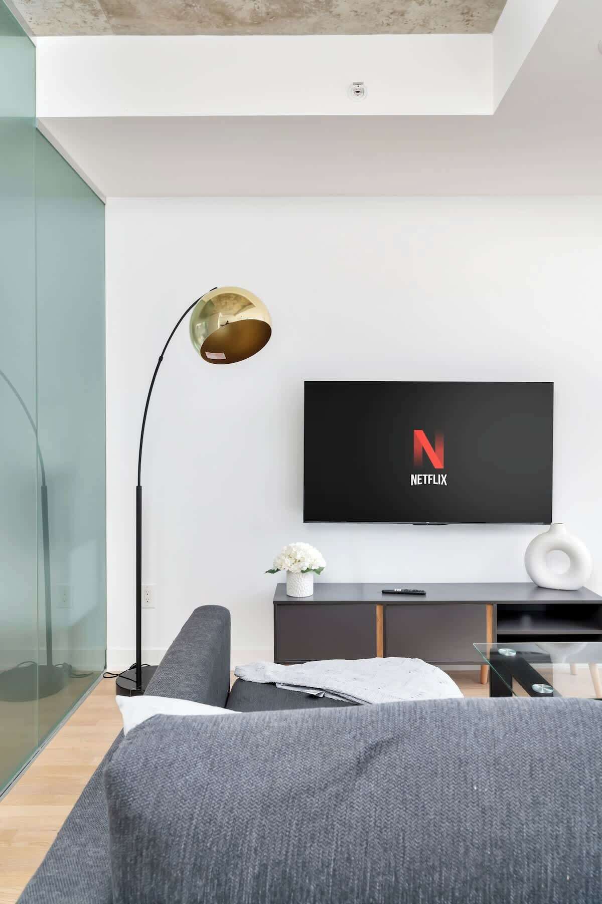 A modern living room with a flat-screen TV mounted on the wall, a floor lamp, and a sofa.