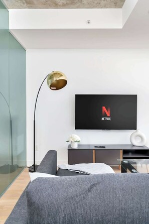 A modern living room with a flat-screen TV mounted on the wall, a floor lamp, and a sofa.
