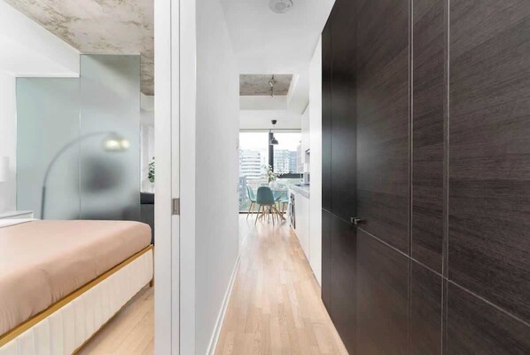 A modern interior with a bed, a dark wooden door, and a view of a dining area with chairs and a table.