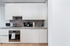 A modern kitchen with white cabinets, a microwave, a coffee maker, and a sink. - Chic City Oasis with Cafes & Bars at your Doorstep! (Toronto)