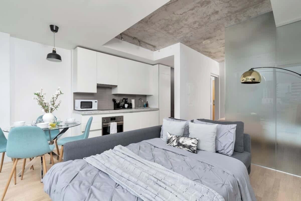 Un dormitorio moderno con una cama grande, un comedor con mesa y sillas, y una kitchenette.