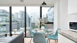 A modern kitchen with a large window, a dining area with a glass table, and a sofa. - Chic City Oasis with Cafes & Bars at your Doorstep! (Toronto)