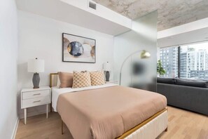 A modern bedroom with a bed, bedside table, lamp, and a city view. - Chic City Oasis with Cafes & Bars at your Doorstep! (Toronto)