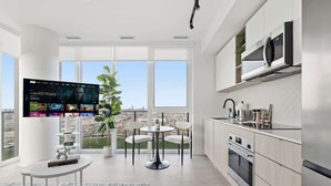 A modern kitchen with a large window, a dining area with a round table, and a flat-screen TV displaying a movie.