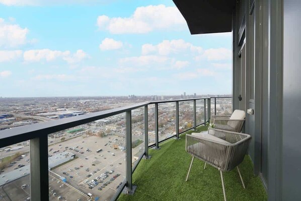 A balcony with a view of a parking lot and cityscape, featuring two wicker chairs.