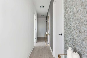 A hallway with a wooden floor, a white door, and a textured wall on the right.
