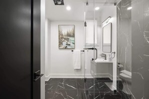 A modern bathroom with a glass shower enclosure, a white sink, and a toilet. - Elegant 2BR Retreat, Sleek Design & Comfort | Parking Available (Toronto)