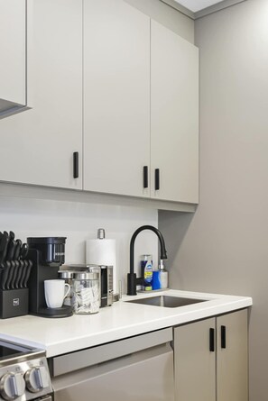 Eine moderne Küche mit weißen Schränken, einer Kaffeemaschine, einem Wasserkocher und einem Spülbecken.
