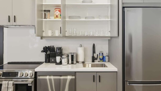 A modern kitchen with stainless steel appliances, a built-in oven, a coffee maker, and a sink. - Elegant 2BR Retreat, Sleek Design & Comfort (Toronto)