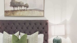 A bedroom with a tufted headboard, a bed with white bedding, green pillows, a side table with a lamp, and a painting above the bed. - Elegant 2BR Retreat, Sleek Design & Comfort (Toronto)