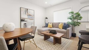 A modern living room with a sofa, coffee table, and a dining area with a table and chairs. - Elegant 2BR Retreat, Sleek Design & Comfort (Toronto)