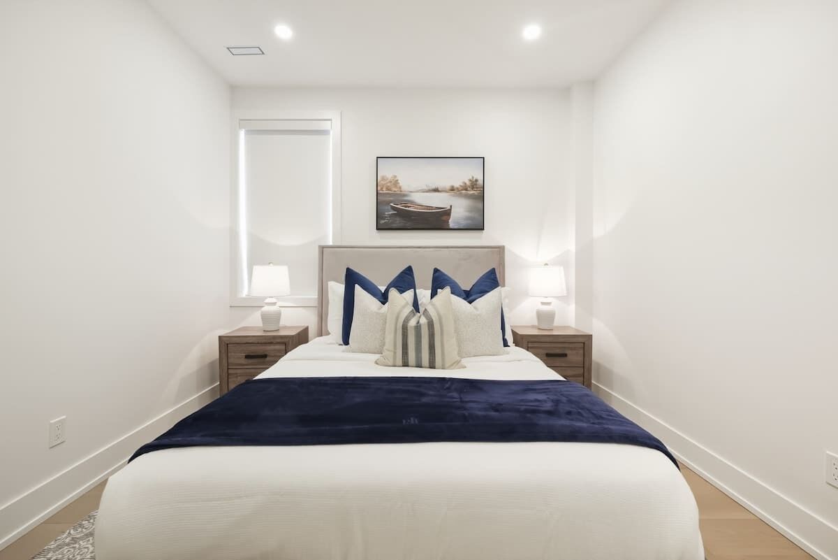 A bedroom with a bed, two bedside tables, a nightstand, a wall-mounted picture, and a window.