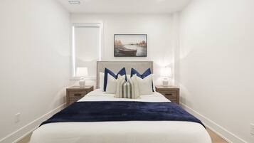 A bedroom with a bed, two bedside tables, a nightstand, a wall-mounted picture, and a window.