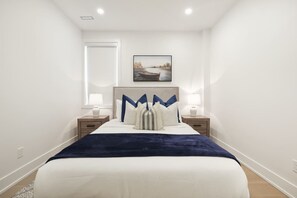 A bedroom with a bed, two bedside tables, a nightstand, a wall-mounted picture, and a window.