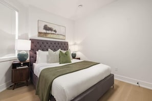 A bedroom with a tufted headboard, a bed with white linens, a green throw blanket, and two bedside tables with lamps. - Elegant 2BR Retreat, Sleek Design & Comfort | Parking Available (Toronto)