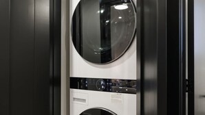 A compact, modern laundry room with two wall-mounted washing machines and a small shelf with a detergent bottle. - Elegant 2BR Retreat, Sleek Design & Comfort (Toronto)