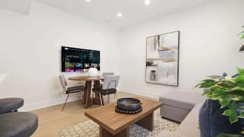 A modern living room with a flat-screen TV, a dining table, and a sofa.
