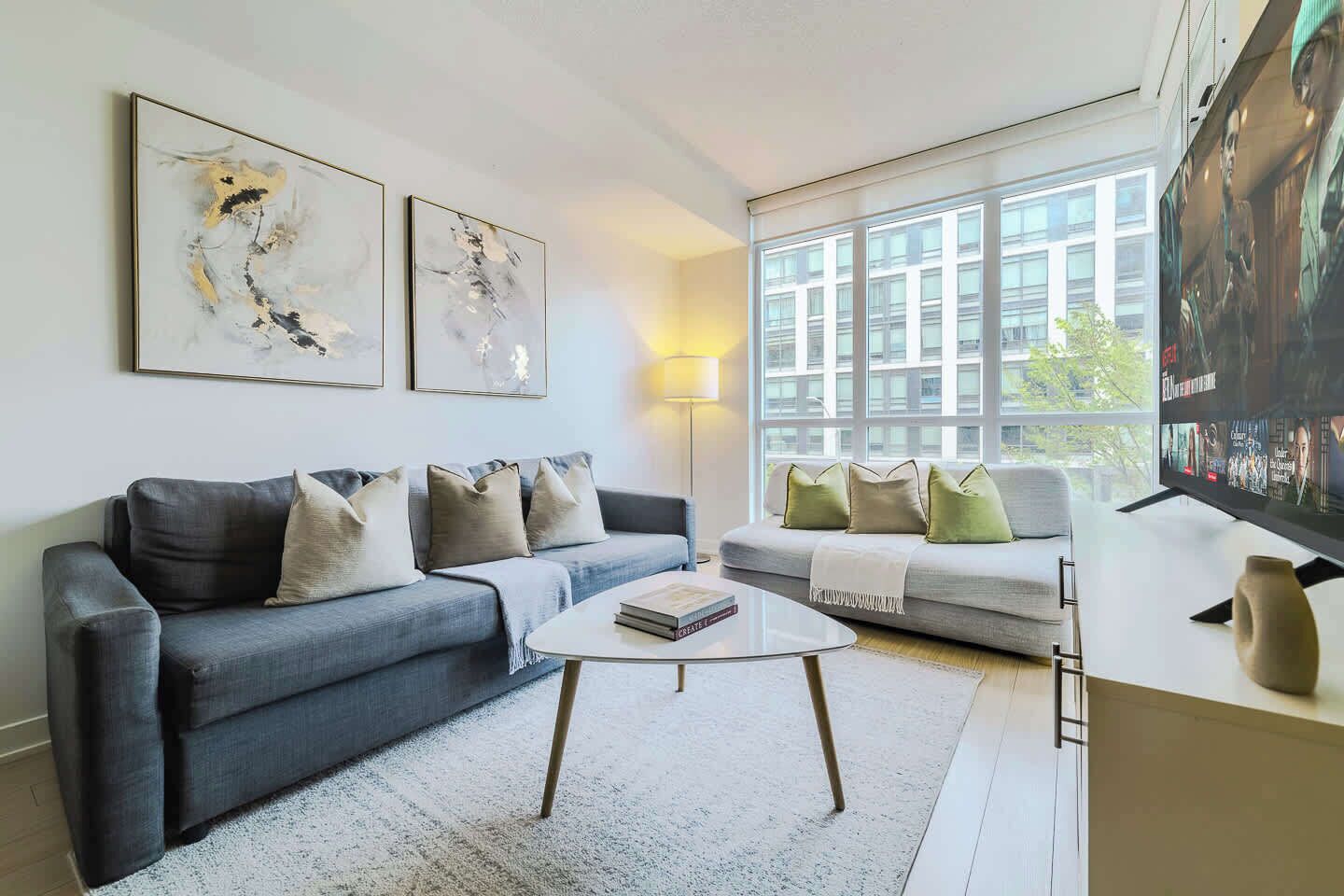 A modern living room with a grey sofa, a white coffee table, and a television on a stand.