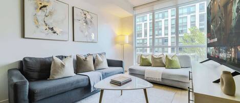 A modern living room with a grey sofa, a white coffee table, and a television on a stand.