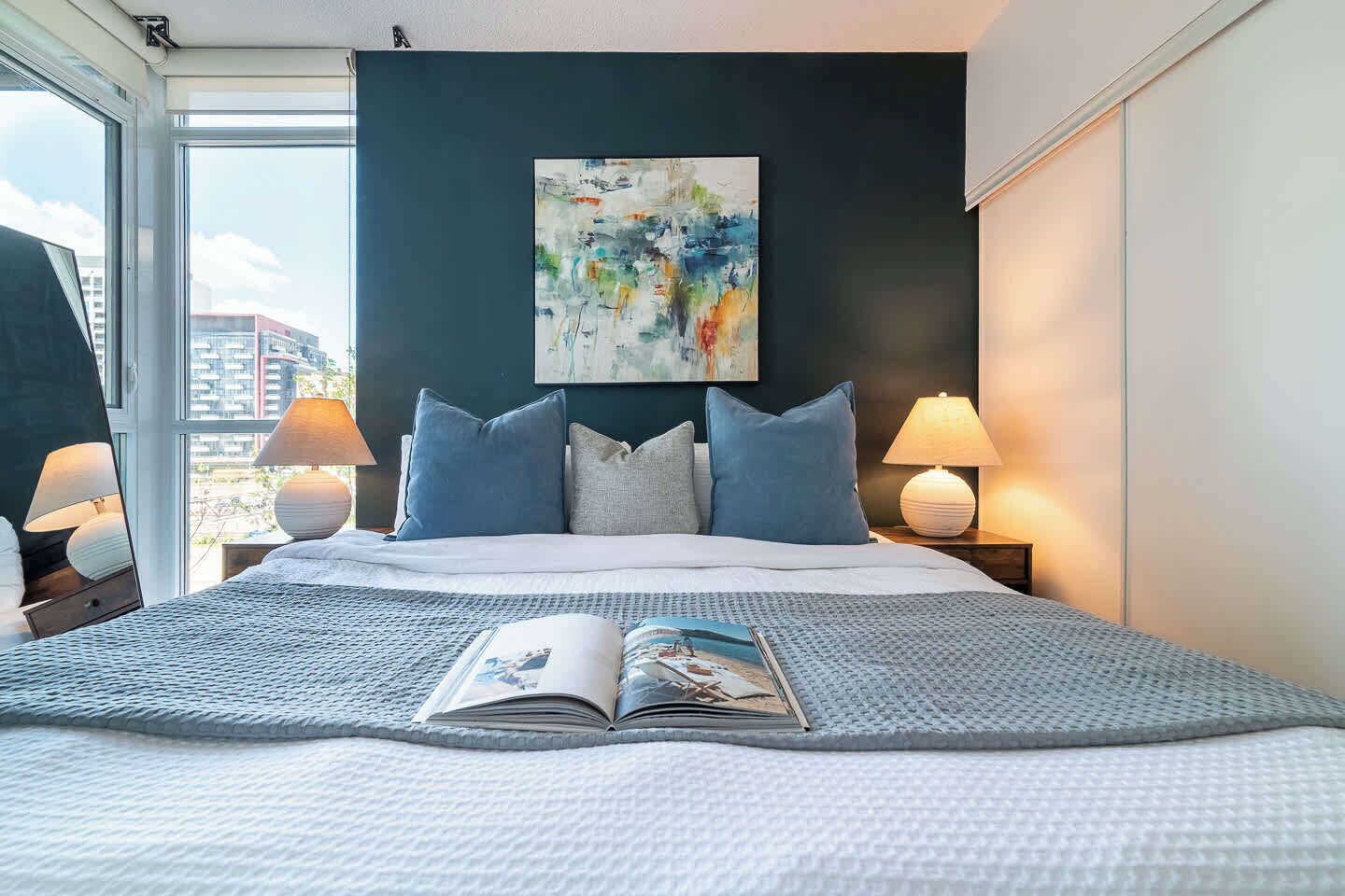 Ein Hotelzimmer mit einem großen Bett, zwei Nachttischlampen, einem Fenster mit Blick und einem Bild an der Wand.