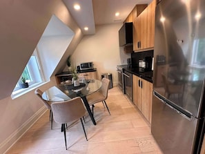 A modern kitchen with a dining area, featuring a glass table, wooden cabinets, and a stainless steel refrigerator.