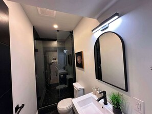 Une salle de bain moderne avec une douche à parois de verre, un grand miroir et un lavabo blanc.